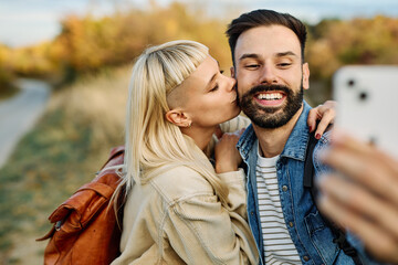 Hiking couple enjoys nature  and takes a selfie photo with a mobile phone  in a lush forest during a sunny day