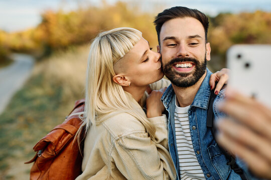 Hiking couple enjoys nature and takes a selfie photo with a mobile phone in a lush forest during a sunny day