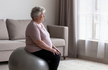 Thoughtful Senior Woman Sits on Exercise Ball Gazing Out Window at Home. Wellbeing and Active Lifestyle