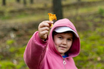 Boy showing edible mushroom he found in the forest. Enthusiastic smiling little child with chanterelle mushroom in his hand. Focus on the mushroom. Weekend fun family activity.