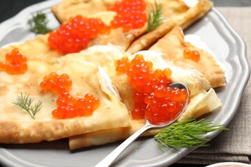 Delicious crepes with red caviar, sour cream and dill on table, closeup