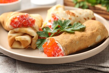Tasty crepes with red caviar, sour cream and parsley on grey table, closeup