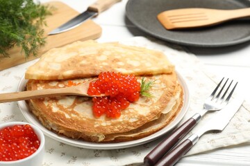 Tasty crepes with red caviar and dill on white wooden table, closeup