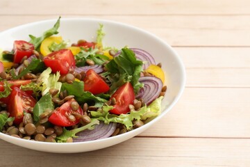 Delicious salad with lentils and vegetables on light wooden table, closeup. Space for text