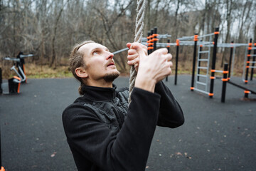 caucasian male practicing obstacle course training, man exercises outdoors on metal bars during...