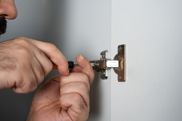 Close-up of hands adjusting a metal cabinet hinge. Perfect for home repair, carpentry, furniture installation and DIY tutorials. 