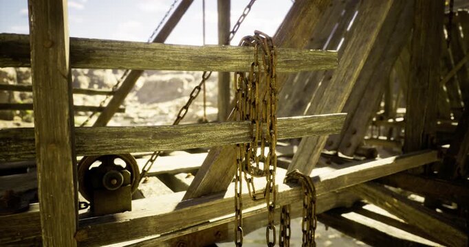Wooden beams and rusty chains create a rugged scene, illuminated by bright sunlight. A rugged, arid landscape fills the background, enhancing the rustic atmosphere.
