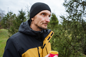 caucasian man holding red mug, profile view with beanie and yellow jacket, contemplative look...