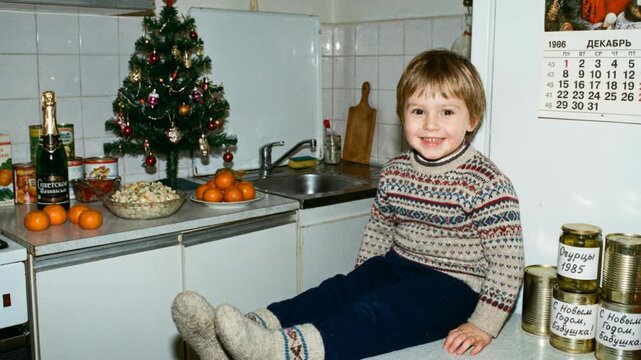 Smiling boy sitting on kitchen counter with 1986 calendar and holiday food