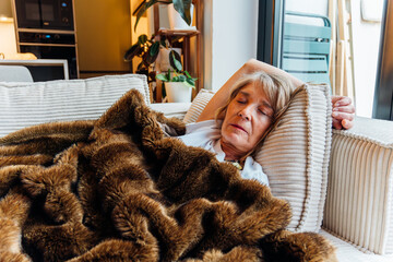 Senior woman relaxing on a comfortable couch, taking a nap under a soft blanket, enjoying quiet time and peaceful rest in a cozy home environment