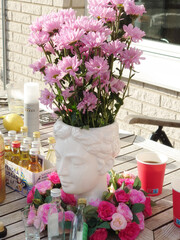 An outdoor wooden table is set with street party essentials: small bottles of alcohol, paper cups, a lime, and flowers in a vase.