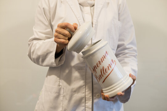 A person in a lab coat opens a large, white ceramic pharmacy jar clearly labeled with the historical ingredient "sperma ballena" (spermaceti) in red script.