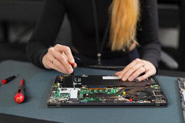 Female IT technician repairing a laptop with screwdriver, open motherboard, performing hardware maintenance and troubleshooting