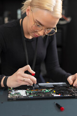 Young female IT technician repairs a laptop with precision and focus in a workshop setting