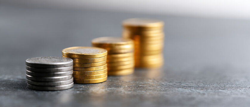 Stacks of silver and gold coins arranged in ascending order on a textured surface with shallow depth of field and blurred background