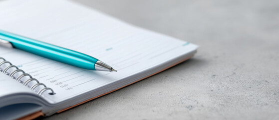 Close-up of a turquoise pen resting on an open spiral-bound planner on a gray textured surface with shallow depth of field