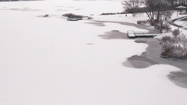 4K Aerial View of a Frozen Suburban Lake Shoreline with Snow-Covered Docks and Benches in Orland Park, Illinois