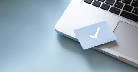 Close-up of a laptop keyboard with a blue card featuring a white checkmark symbol placed on the edge, set against a smooth light blue background