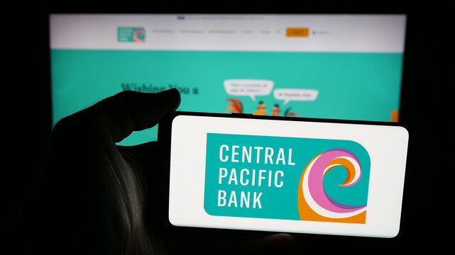 Stuttgart, Germany - 11-26-2025: Person holding mobile phone with logo of financial company Central Pacific Bank (CPB) on screen in front of web page. Focus on phone display.