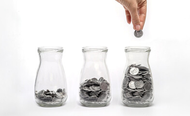 Three glass jars filled with coins at different levels, hand adding coin. Financial growth, savings.
