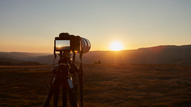 Landscape photography. A camera on a tripod against a backdrop of mountains in the last rays of the setting sun.