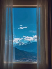 Fototapeta premium Stunning Alpine Vista Through an Open Window: Vertical View of Snow-Capped Mountains and a Blue Valley Town Framed by Flowing Sheer Curtains in a Hotel or Home Setting