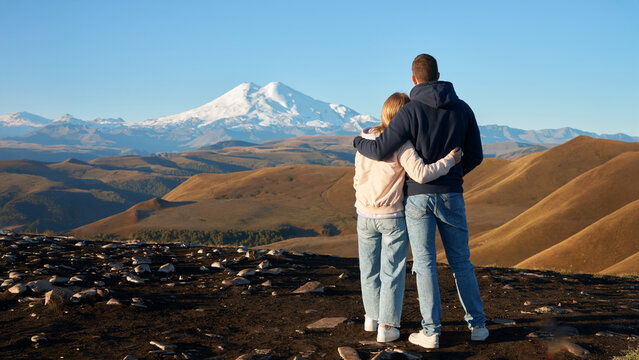 A young couple on a viewing platform against the backdrop of autumn mountains and the majestic snow-capped Elbrus early in the morning. Copy space.