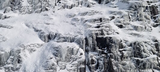 Snow-covered rock face showing frozen waterfalls in a remote mountain landscape during winter