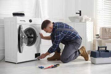 Repairman examining broken washing machine at home