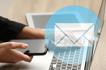 Email notification. Man using laptop and mobile phone at table, closeup. Letter coming from screen