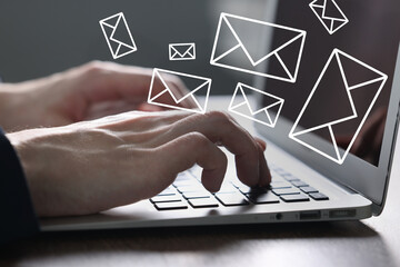 Man sending or receiving email on laptop at table, closeup. Letters flying out of screen