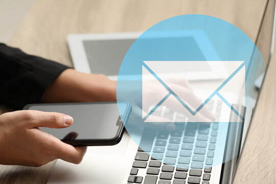 Email notification. Man using laptop and mobile phone at table, closeup. Letter coming from screen