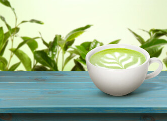 Matcha latte in cup on wooden table against green leaves. Space for text