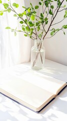 An open notebook sits on a white table next to a vase of greenery, bathed in bright sunlight.