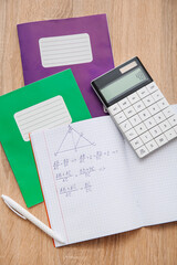 Naklejka premium Open copybook with formulas, calculator and pen on wooden table