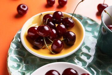 Plate with sweet cherries on orange background