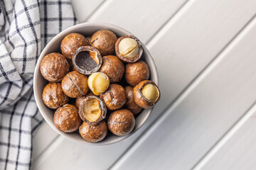 Tasty macadamia nuts in bowl on white table.