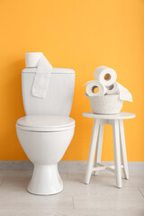 Ceramic toilet bowl and rolls of paper near color wall