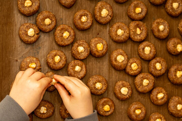 Top view of child's hands pressing hazelnuts into raw cookie dough. Preparing traditional Christmas...