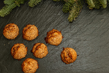 Overhead flat lay view of homemade coconut macaroon cookies arranged on a dark textured slate background decorated with green pine branches