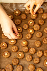 Top view of mother and child hands placing hazelnuts on raw cookie dough together. Family holiday baking tradition