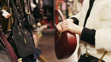 Female hands examining stylish purse options inside a modern boutique store.