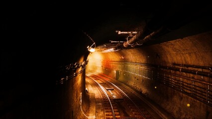 Warm lights illuminate the tracks as they curve into the unknown. Rusty walls reflect the glow, creating an atmosphere of intrigue and adventure deep underground.