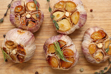 Fototapeta premium Baked garlic with peppercorns, rosemary and thyme on wooden board