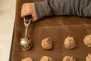 Close up of a child's hand holding a metal scoop to portion coconut cookie dough onto a baking mat. Holiday baking