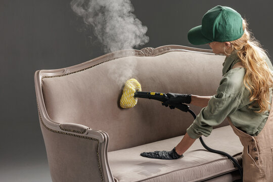 Steam mop disinfecting upholstered sofa backrest during home cleaning