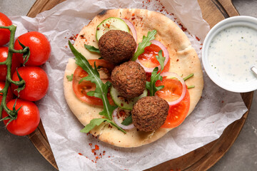 Wooden board of delicious pita with falafel and fresh vegetables on grey background, closeup