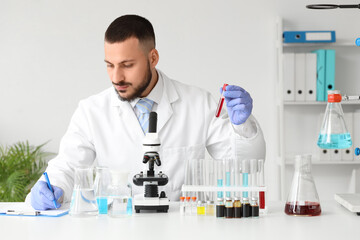 Male scientist with blood sample and microscope working in laboratory