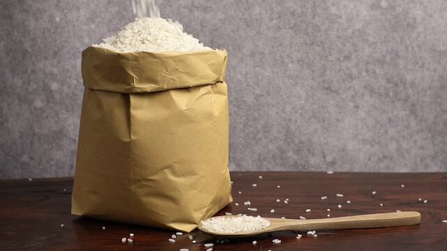Close-up footage of white rice being poured into a paper bag, showing falling grains clearly for cooking, donation, or zakat fitrah themes.