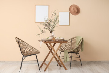 Fototapeta premium Elegant table setting with plates, glasses and blooming tree branches near beige wall